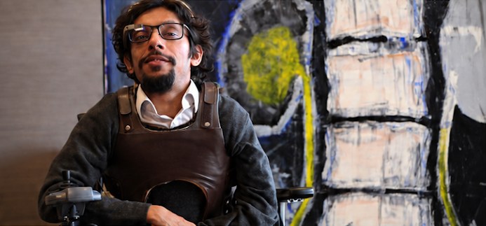 Davey Jose in his wheelchair, wearing a body brace, in front of a large abstract canvas of a spine