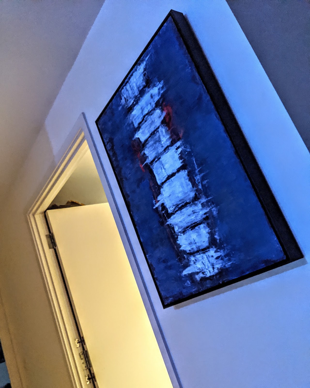 A framed oil painting of a spinal column in blue, white and red, hanging on a wall