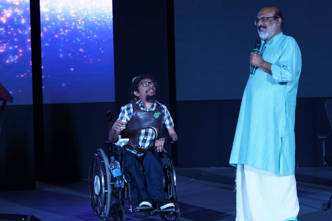 Davey Jose speaking on stage beside a guest at the Centre for Differently Abled in Kerala