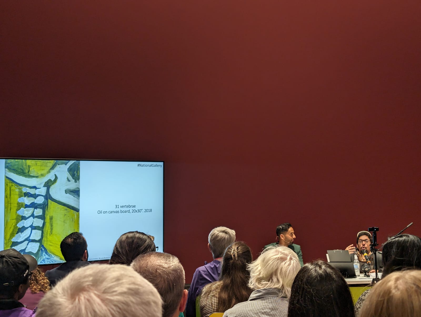 Davey Jose speaking beside a projected image of his 31 vertebrae painting at the National Gallery