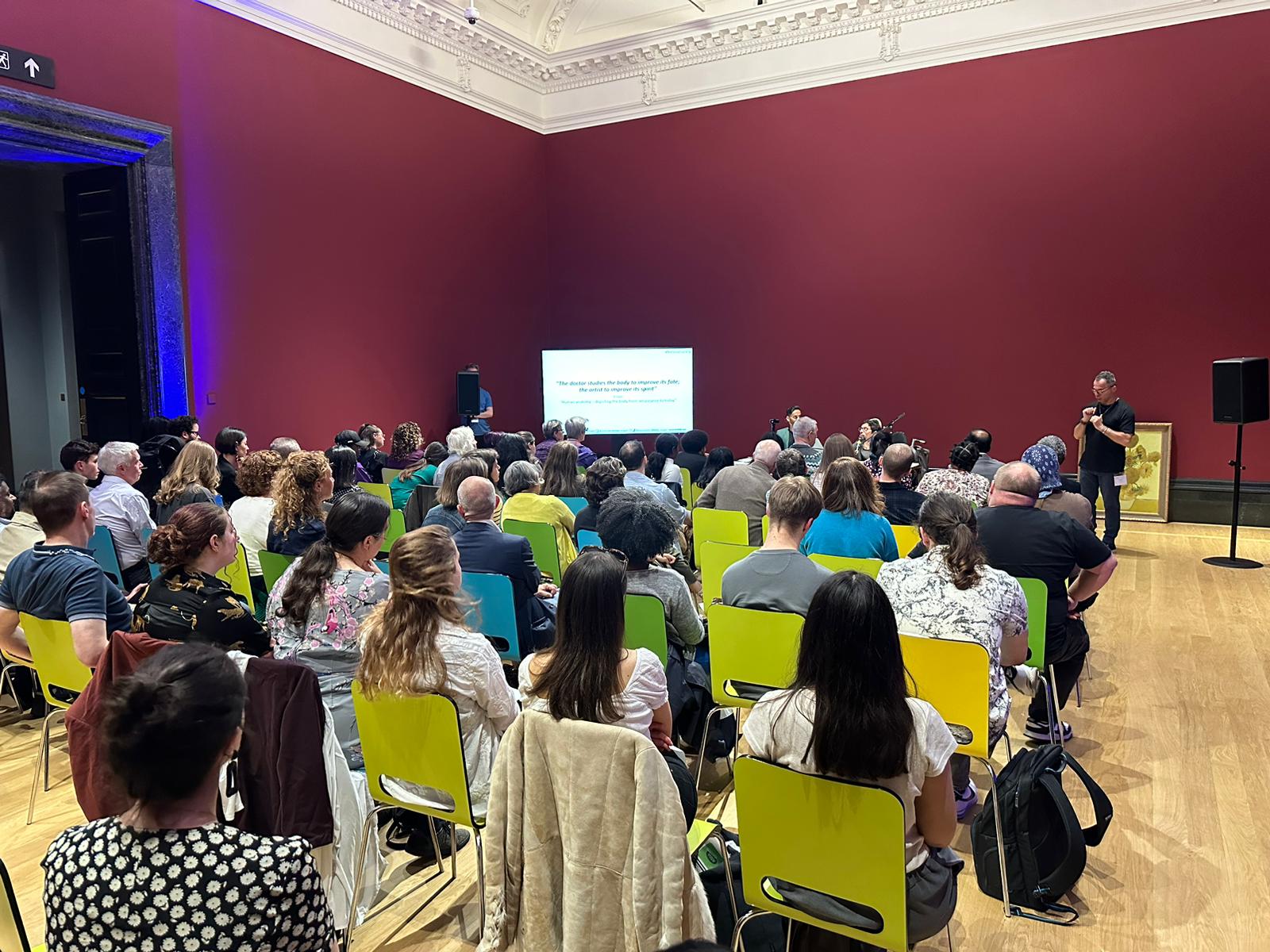A full audience listens during Davey Jose’s National Gallery talk in a red-walled gallery room